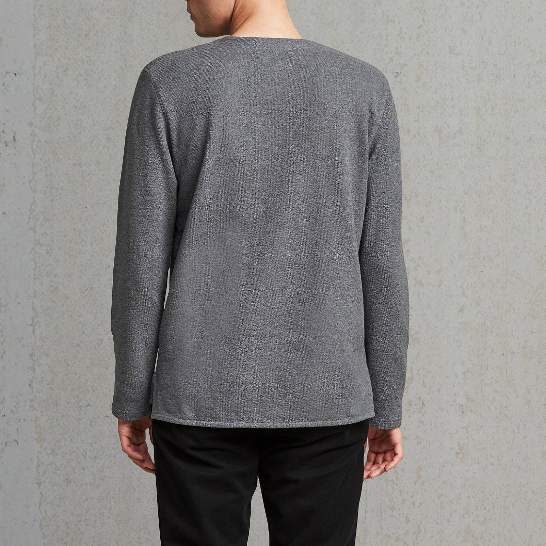 Man wearing a gray long-sleeve shirt against a plain wall