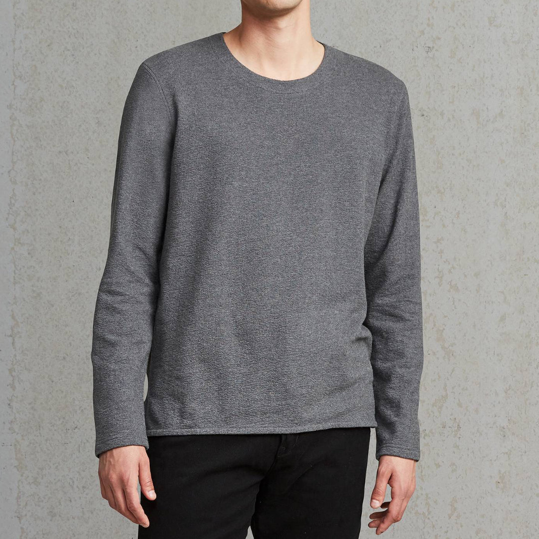 Man wearing a gray sweater and black pants against a plain background
