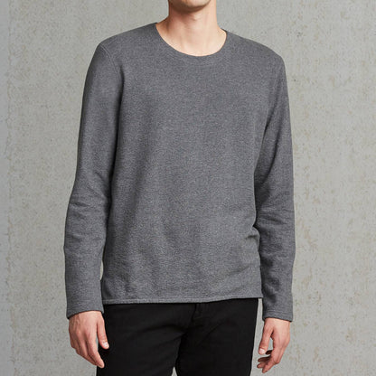 Man wearing a gray sweater and black pants against a plain background