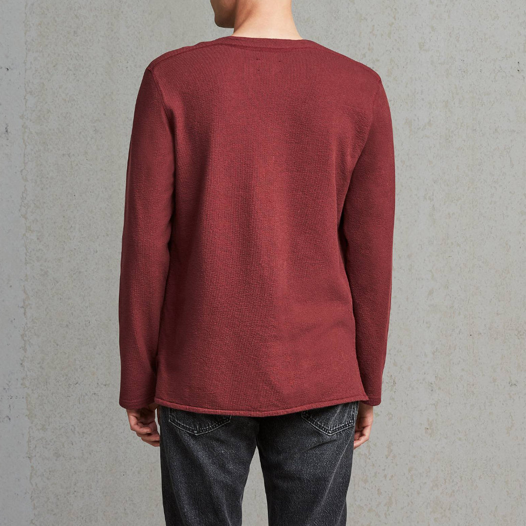Man wearing a red sweater and dark jeans against a gray wall