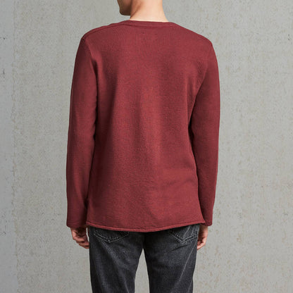 Man wearing a red sweater and dark jeans against a gray wall