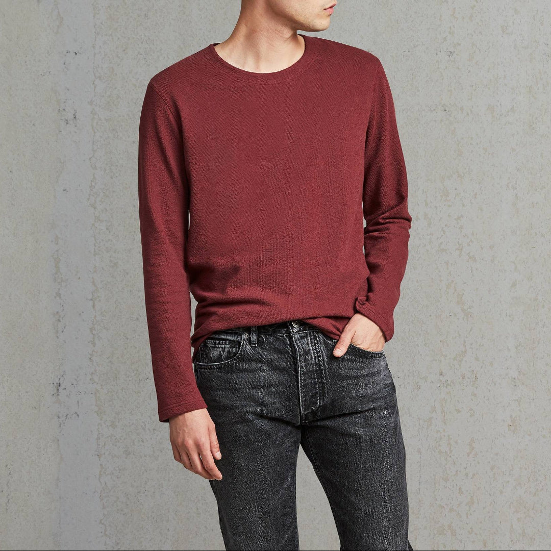 Man wearing a maroon sweater and dark jeans against a gray background