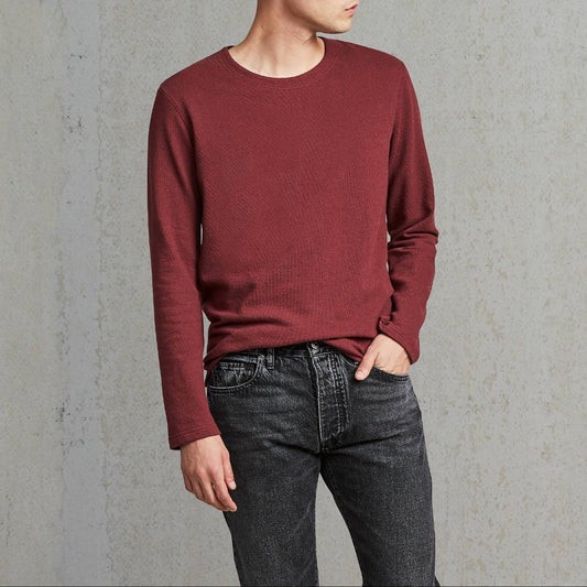 Man wearing a maroon sweater and dark jeans against a gray background