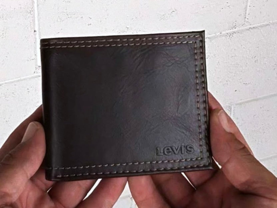 Brown leather wallet with 'Levi's' branding held by a person against a light-colored brick wall.