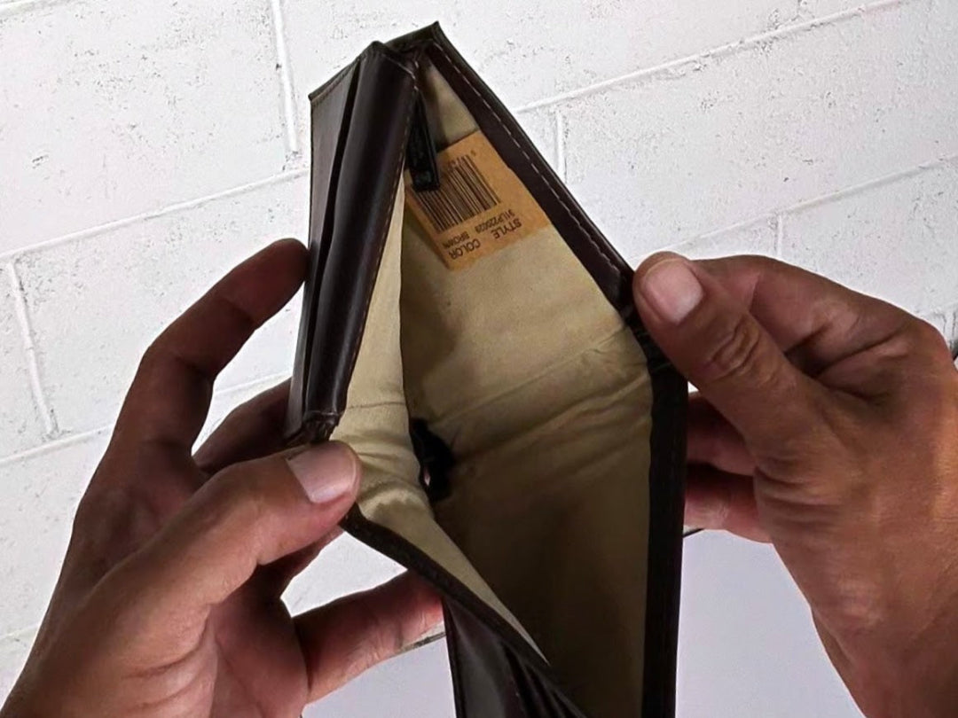 Brown leather wallet being held open to reveal a beige interior on a white brick wall background.