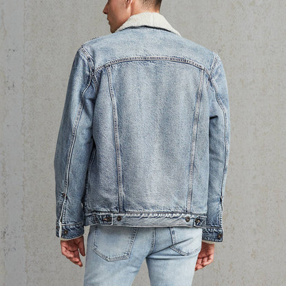 Man wearing a light blue denim jacket and jeans against a gray background