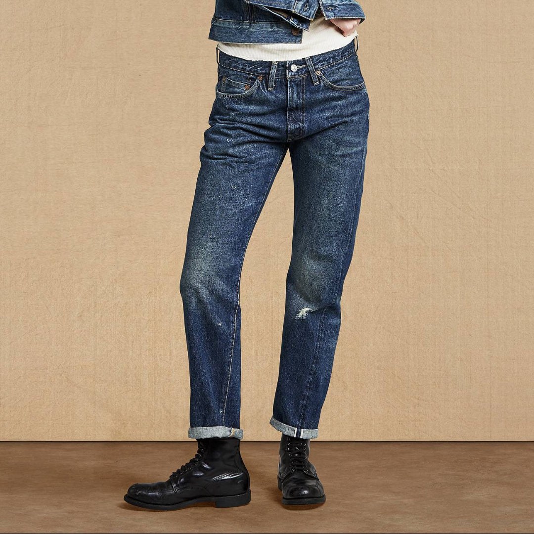 Woman wearing a denim jacket and jeans standing against a beige background