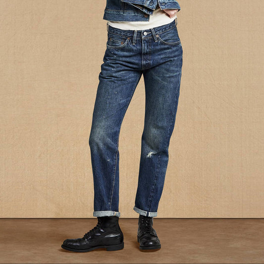 Woman wearing a denim jacket and jeans standing against a beige background