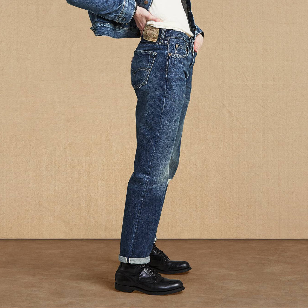 Person wearing a blue denim jacket and jeans standing against a beige background
