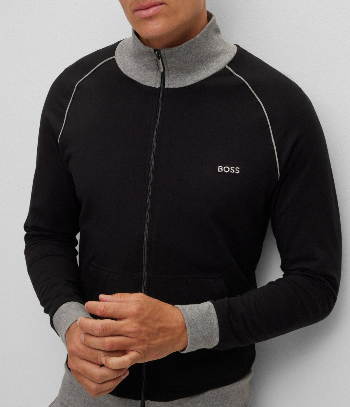Man wearing a black and gray jacket with a visible brand logo on a light gray background