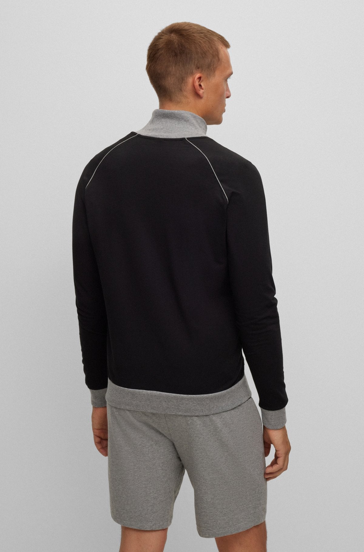 Person wearing a black long-sleeve shirt and gray shorts on a light gray background