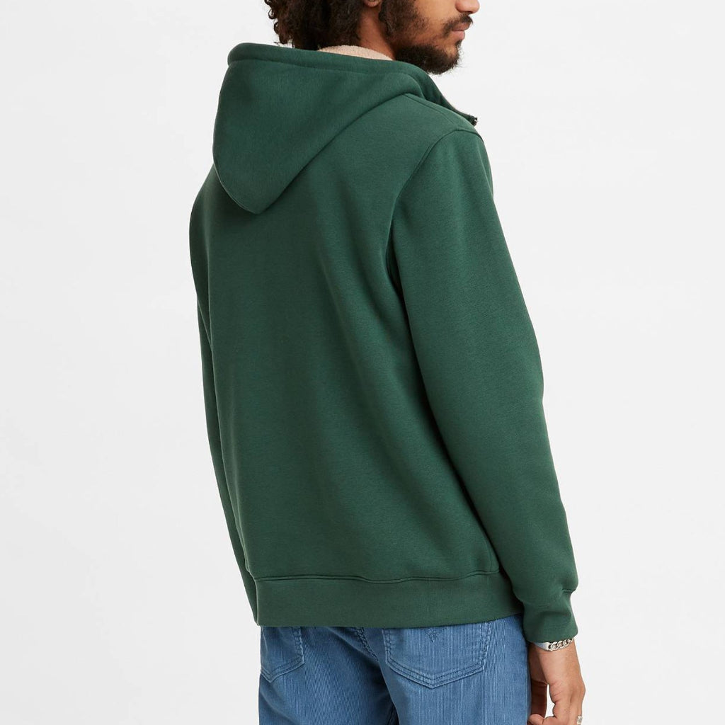 Man wearing a green hoodie and blue pants on a white background