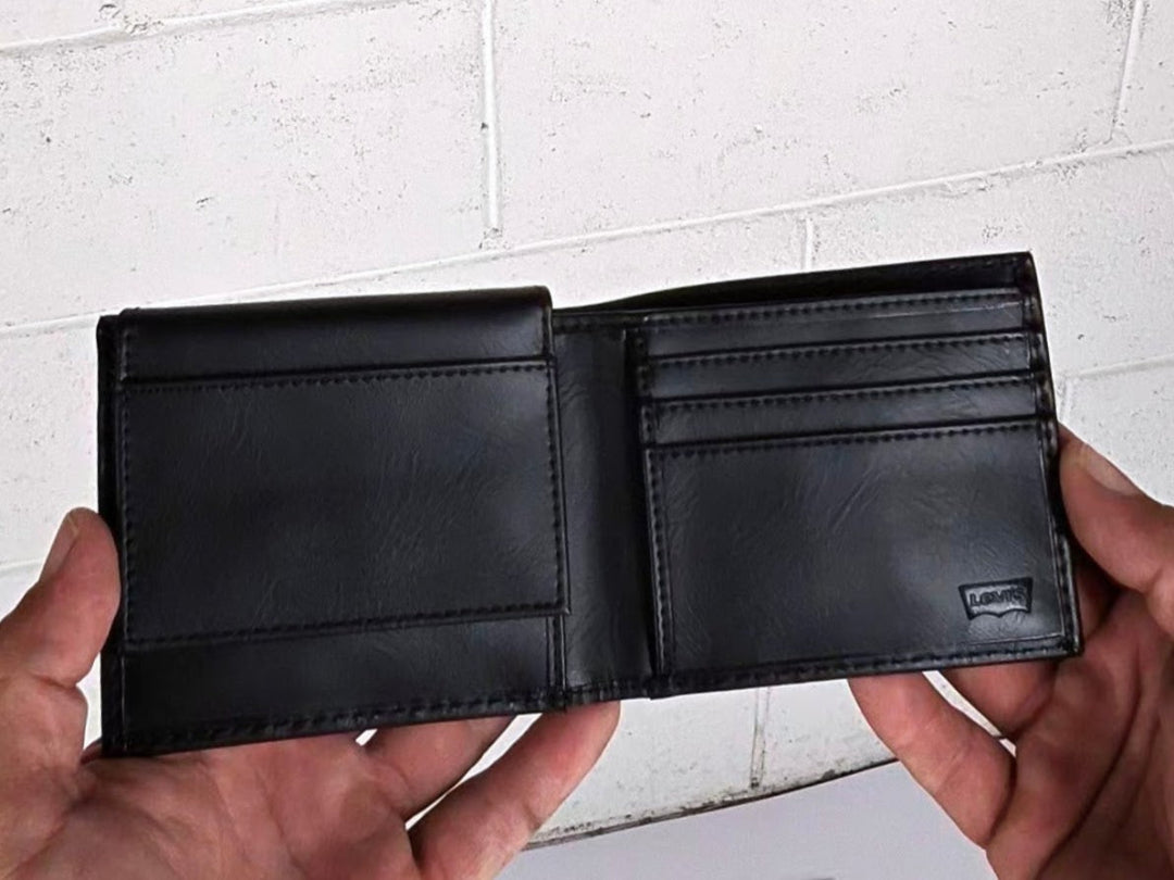 Black leather wallet held open by hands against a white brick wall background