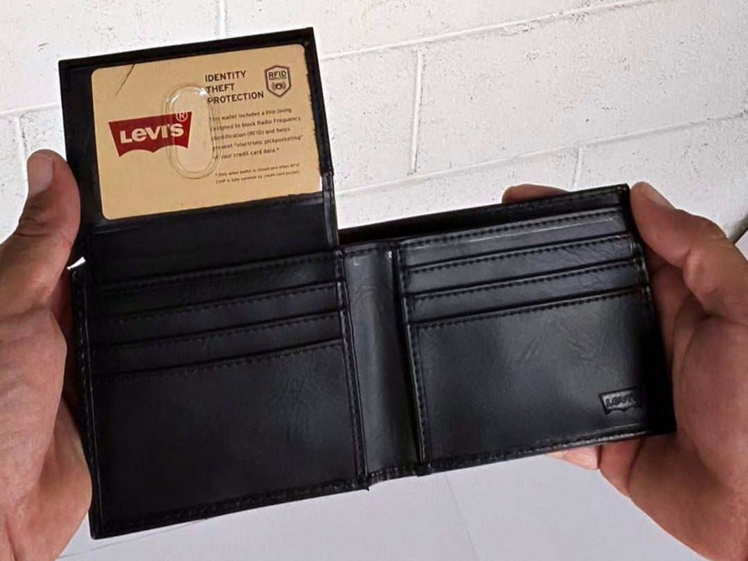 Black leather wallet held open by hands with a Levi's card inside, on a white brick wall background.