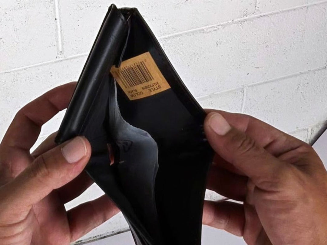 Black wallet with a visible brand tag held by hands against a white tiled wall.